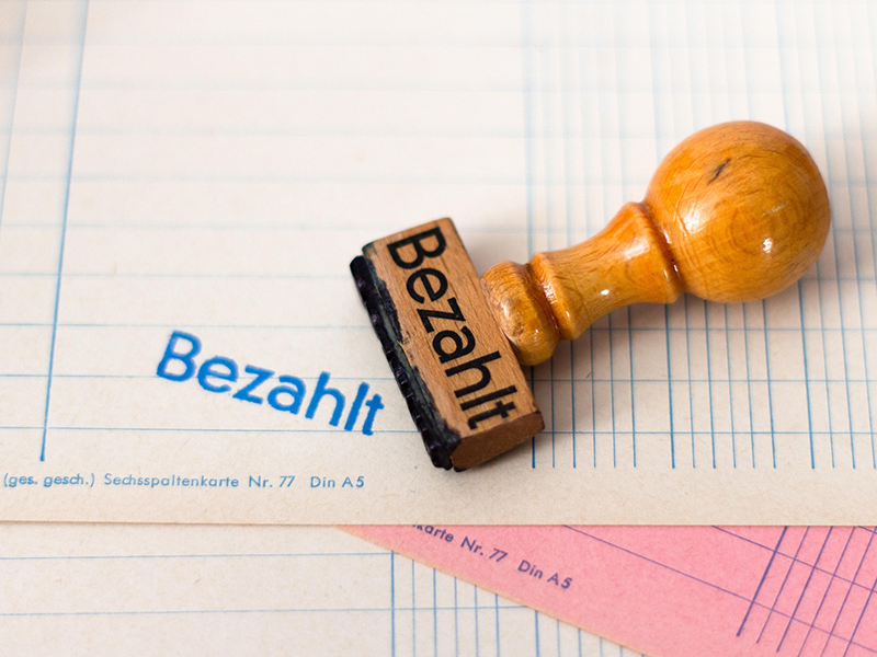 Papiere mit einem Stempelabdruck "Bezahlt" und dem dazugehörigen Holzstempel